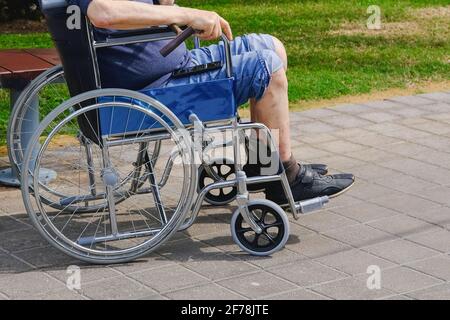 Homme âgé avec diabète et maladie rénale assis sur un fauteuil roulant marchant avec un assistant dans le parc. Banque D'Images