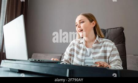 Femme apprend de la musique chantant des voix jouant du piano en ligne à l'aide d'un ordinateur portable à l'intérieur de la maison. Adolescente chante chanson jouer piano synthétiseur pendant l'étalonnage vidéo Banque D'Images