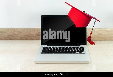 Concept d'éducation en ligne ou de remise des diplômes avec un ordinateur portable sur un bureau en bois avec casquette rouge Banque D'Images