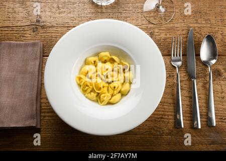 Vue de dessus d'un bol de délicieux pâtes cappellettis avec bouillon placé sur une table en bois près de la serviette et des couverts Banque D'Images