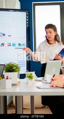 Une femme dirigeante dirige l'animateur en donnant une présentation financière dans une salle de réunion moderne pour le groupe des employés de l'entreprise, un mentor explique l'équipe professionnelle de formation lors d'un séminaire d'affaires Banque D'Images