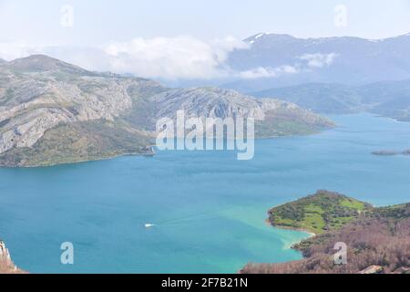 Vue aérienne du réservoir de Riaño avec un bateau naviguant dans ses eaux bleu turquoise entourées de montagnes au printemps. Image de nature verte, vie idyllique Banque D'Images