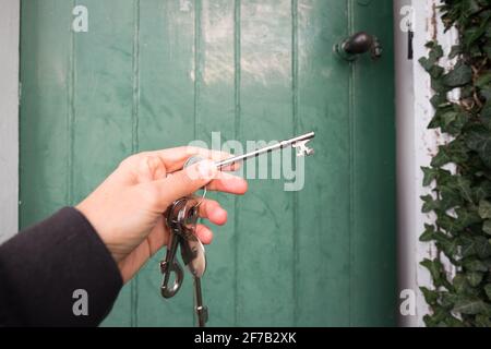Main tenant les clés à l'ancienne à la porte verte de la maison - propriétaire, maison d'achat ou de location concept Banque D'Images