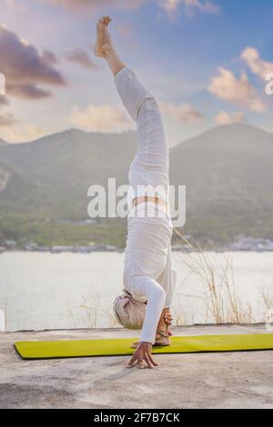 Kundalini yoga femme en vêtements blancs et turban pratique le yoga kundalini sur le fond de la mer, des montagnes et du coucher du soleil. Peinture de visage de combat Banque D'Images