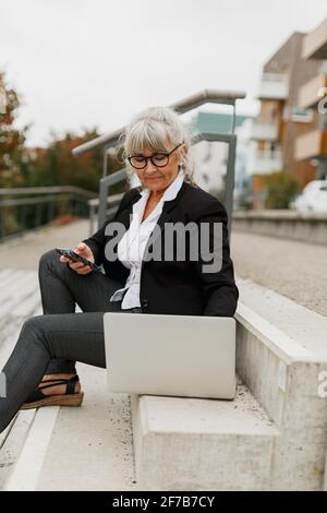 Femme âgée utilisant un ordinateur portable dans les escaliers Banque D'Images
