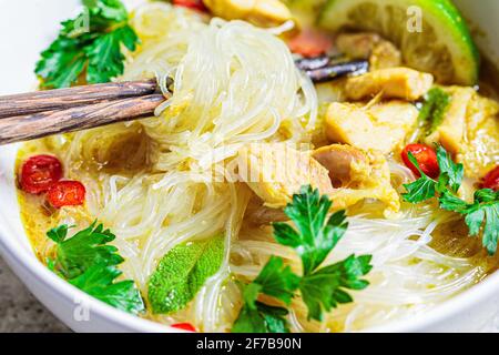 Soupe de poulet au curry vert thaïlandais avec nouilles, piment et herbes dans un bol blanc. Banque D'Images