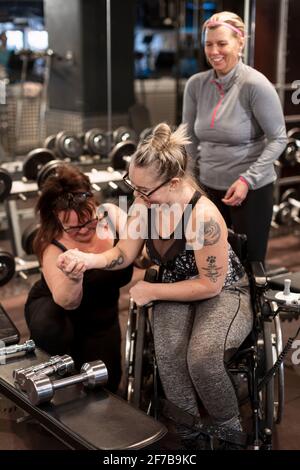 Femme en fauteuil roulant en salle de gym avec entraîneur personnel Banque D'Images