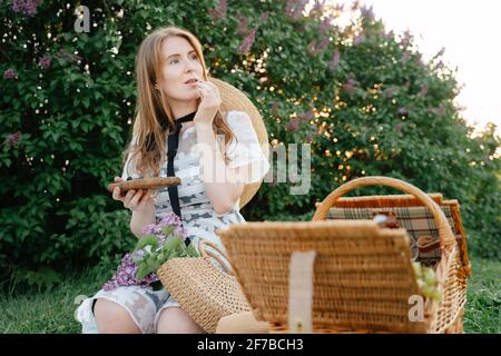 Une jeune fille en pique-nique mange des bleuets frais tout en étant assise sur l'herbe verte dans le parc. Banque D'Images