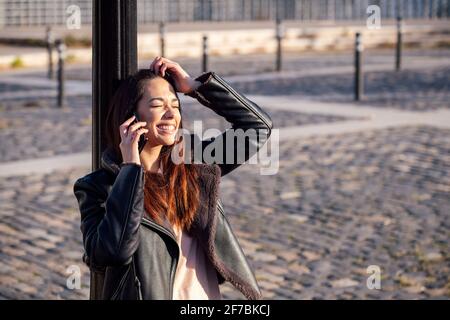 jeune femme riant et parlant au téléphone se penchant contre un lampadaire, concept de technologie et de style de vie urbain, copyspace pour le texte Banque D'Images