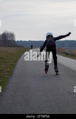 Accident sportif, trébucher tandis que des skytes en ligne, une fille est à l'intérieur. Vue arrière juste avant l'automne. Le casque et les protections sont importants. Banque D'Images