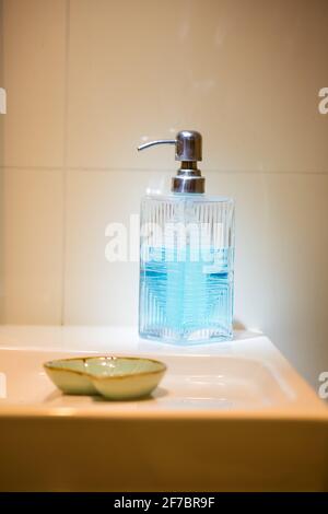 Distributeur de savon en verre sur un lavabo blanc, idées de design d'intérieur pour les salles de bains. Éclairage extravagant. Banque D'Images