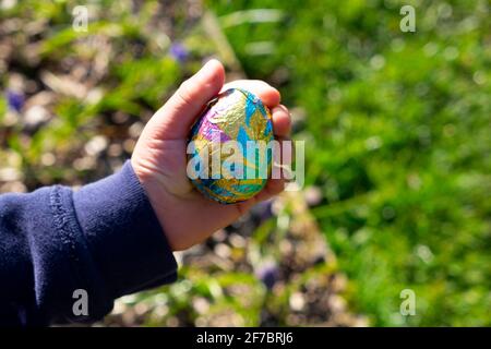 Main d'un enfant garçon de 4 ans tenant un œuf de chocolat coloré Dans le jardin de campagne sur une chasse aux oeufs de Pâques Carmarthenshire pays de Galles Royaume-Uni Grande-Bretagne KATHY DEWITT