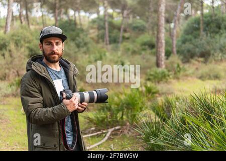 Homme photographe avec un appareil photo reflex numérique dans ses mains posant dans la forêt Banque D'Images