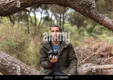 Photographe professionnel assis dans un arbre avec son appareil photo sa main regarde tout droit Banque D'Images