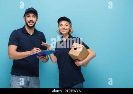 messagerie joyeuse tenant le colis et pointant vers l'écriture d'un collègue arabe ordre sur presse-papiers isolé sur bleu Banque D'Images