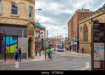 Une rue de la ville qui se courbe au coin de la rue et mène à un pont. Un bâtiment de style gothique est au premier plan et un ciel nuageux est au-dessus. Banque D'Images