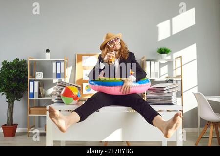 Drôle de travailleur de bureau assis sur le bureau, boire un cocktail et attendre les vacances d'été Banque D'Images