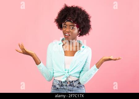 Une jeune femme noire décontentée haussant les épaules debout sur fond rose Banque D'Images
