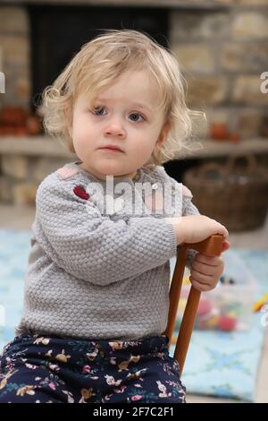 kleines Mädchen sitzt im Wohnzimmer auf einem Kinderstuhl aus Holz - petite fille assise sur une chaise d'enfant en bois séjour Banque D'Images