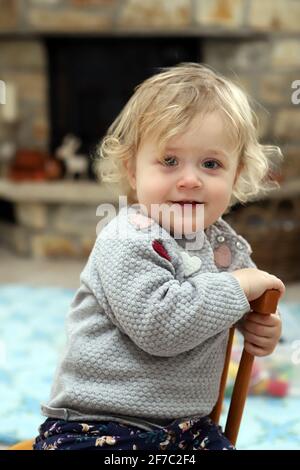 kleines Mädchen sitzt im Wohnzimmer auf einem Kinderstuhl aus Holz - petite fille assise sur une chaise d'enfant en bois séjour Banque D'Images