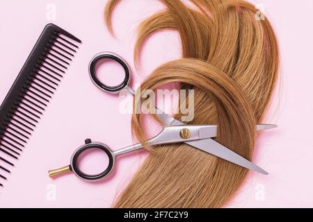 Ciseaux, un peigne et un fil coupé de cheveux blonds femelles pour enfants sur fond rose, vue de dessus, coiffure. Banque D'Images