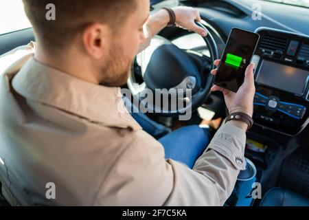 Homme regardant l'indicateur de charge de la voiture électrique via l'application pour smartphone. Niveau de charge de la batterie sur l'écran du téléphone portable Banque D'Images