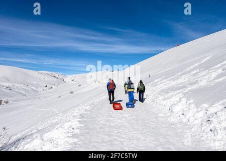 Groupe de randonneurs avec sacs à dos et bobs marchant sur un sentier enneigé sur le plateau de Lessinia, Parc naturel régional, station de ski de Malga San Giorgio, Italie. Banque D'Images