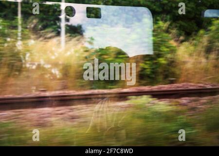 Silhouette de jeune homme passager méconnaissable reflétée dans la fenêtre du train avec paysage vert passant. Transport écologique, environnement Banque D'Images