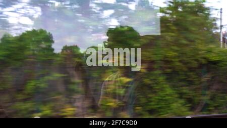 Silhouette de jeune homme passager méconnaissable reflétée dans la fenêtre du train avec paysage vert passant. Transport écologique, environnement sustai Banque D'Images