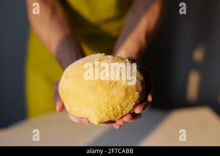 Le boulanger de chef en tablier vert tient dans les mains une boule de pâte faite pour le pain, la pizza ou la tarte. Biscuits maison au four, préparation de la pâtisserie de Pâques ou concept savoureux de biscuit. Photo de haute qualité Banque D'Images