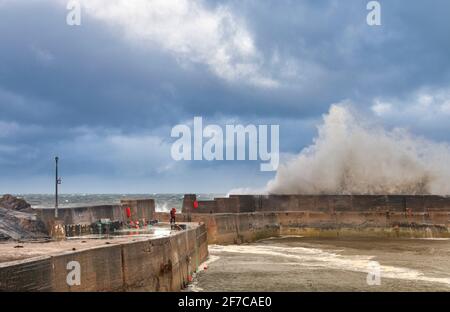 PORTKNOCKIE CÔTE DE MORAY ÉCOSSE UNE TEMPÊTE VIOLENTE ET DES VAGUES TURBULENTES SE BRISENT AU-DESSUS DES MURS DU PORT ET DE L'HOMME SOLITAIRE Banque D'Images