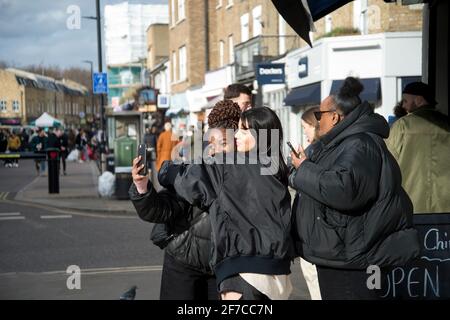 Londres, Angleterre, Royaume-Uni. Hackney. Champs de Londres. Marché de Broadway. Les jeunes femmes prennent des selfies. Banque D'Images
