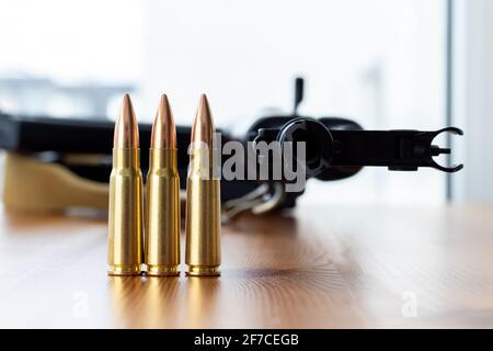 Trois balles contre un fond flou de fusil d'assaut Kalashnikov. Cartouches calibre 7.62 pour ak 47 gros plan. Banque D'Images