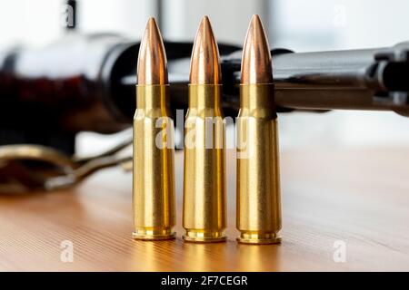 Trois balles contre un fond flou de fusil d'assaut Kalashnikov. Cartouches calibre 7.62 pour ak 47 gros plan Banque D'Images
