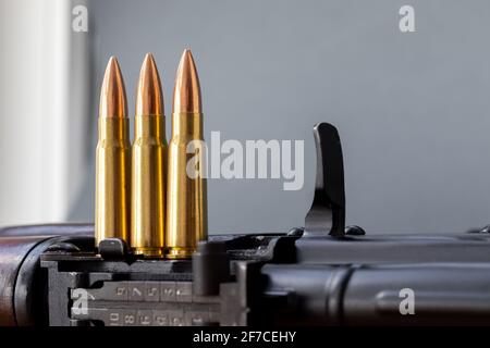 Trois balles sur le fusil d'assaut Kalashnikov sur fond gris flou. Cartouches calibre 7.62 pour ak 47, gros plan, mise au point sélective avec fonction de copie Banque D'Images