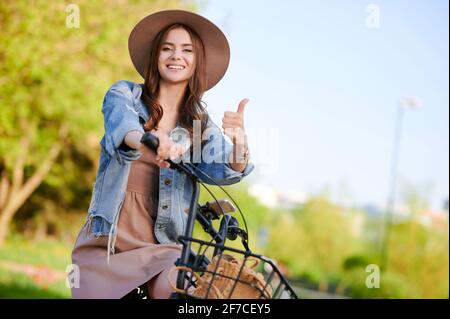 Une jeune femme montre un geste de pouce et se déplace sur le location de vélo en plein air en été Banque D'Images