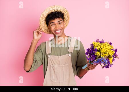 Photo de gai fermier gars tenir le bouquet de fleurs usure de la paille chapeau beige général isolé couleur rose fond Banque D'Images