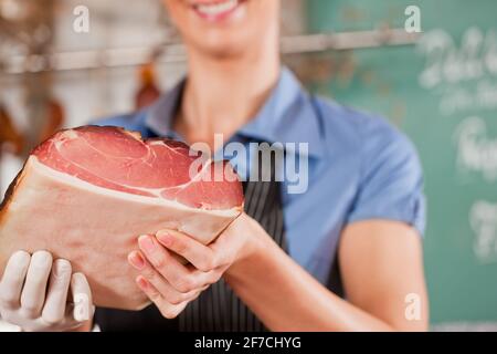 Une jeune femme ou une boucherie avec du jambon cru dans une boucherie; elle est probablement une assistante d'atelier Banque D'Images