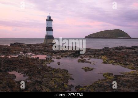 Paysage idyllique coloré de ciel rose coucher de soleil ou lever de soleil à Penmon point et Trywn du Lighthouse le long du rivage rocheux à Anglesey, au nord du pays de Galles, Royaume-Uni. Banque D'Images