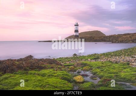 Paysage idyllique coloré de ciel rose coucher de soleil ou lever de soleil à Penmon point et Trywn du Lighthouse le long de la côte rocheuse d'algues vertes à Anglesey, au nord Banque D'Images