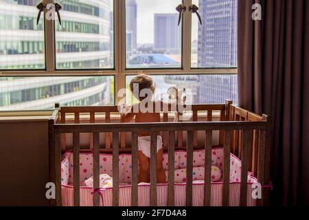 Un Enfant Charmant Donne Sur La Fenetre De La Metropole Tout En Se Tenant Dans Un Lit De Bebe Un Bebe Dans Un Lit De Bebe Donne Sur La Fenetre De La