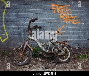 Une moto corrodée pour enfants a été sauvée du Canal de Regen, adochée à un mur avec les mots “Free Bike” peints sur le mur Banque D'Images