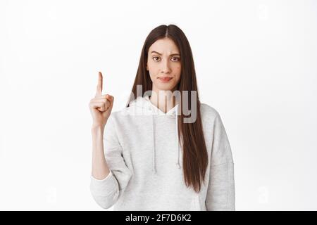 Déçu frowning fille pointant le doigt vers le haut, regardant avec mécontent visage, se plaignant, montrant le mauvais texte promotionnel, scolding, se tenant dessus Banque D'Images