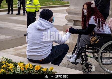 LONDRES, Royaume-Uni - le 3 avril 2021 : un moment doux et sincère capturé par une femme handicapée en fauteuil roulant tient les mains d'un partenaire lors des manifestations Banque D'Images