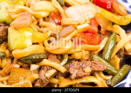 Agneau cuit avec des nouilles de blé et des légumes cuits sur une authentique assiette orientale. Macro. La photo peut être utilisée comme arrière-plan entier. Banque D'Images