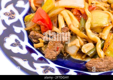 Agneau cuit avec des nouilles de blé et des légumes cuits sur une authentique assiette orientale. Macro. La photo peut être utilisée comme arrière-plan entier. Banque D'Images