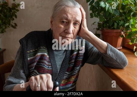 Portrait d'une triste vieille femme solitaire, assise à la maison près de la fenêtre. Vieillesse, problèmes de santé, handicaps. Banque D'Images