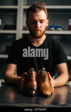 Portrait du cordonnier mâle tient la vieille chaussure en cuir brun clair et les chaussures brillantes réparées après le travail de restauration. Banque D'Images