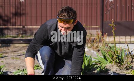 Les jeunes ouvriers du bâtiment se focalisent avec des lunettes jaunes pour éliminer les irrégularités sur la table de plancher et regarder vers le bas. Homme dans le patio et le jardin. Sortie Banque D'Images