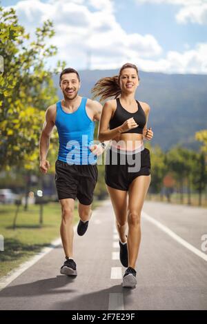 Portrait complet du jeune homme et de la femme qui s'en jogging une voie asphaltée en circulation dans la ville Banque D'Images